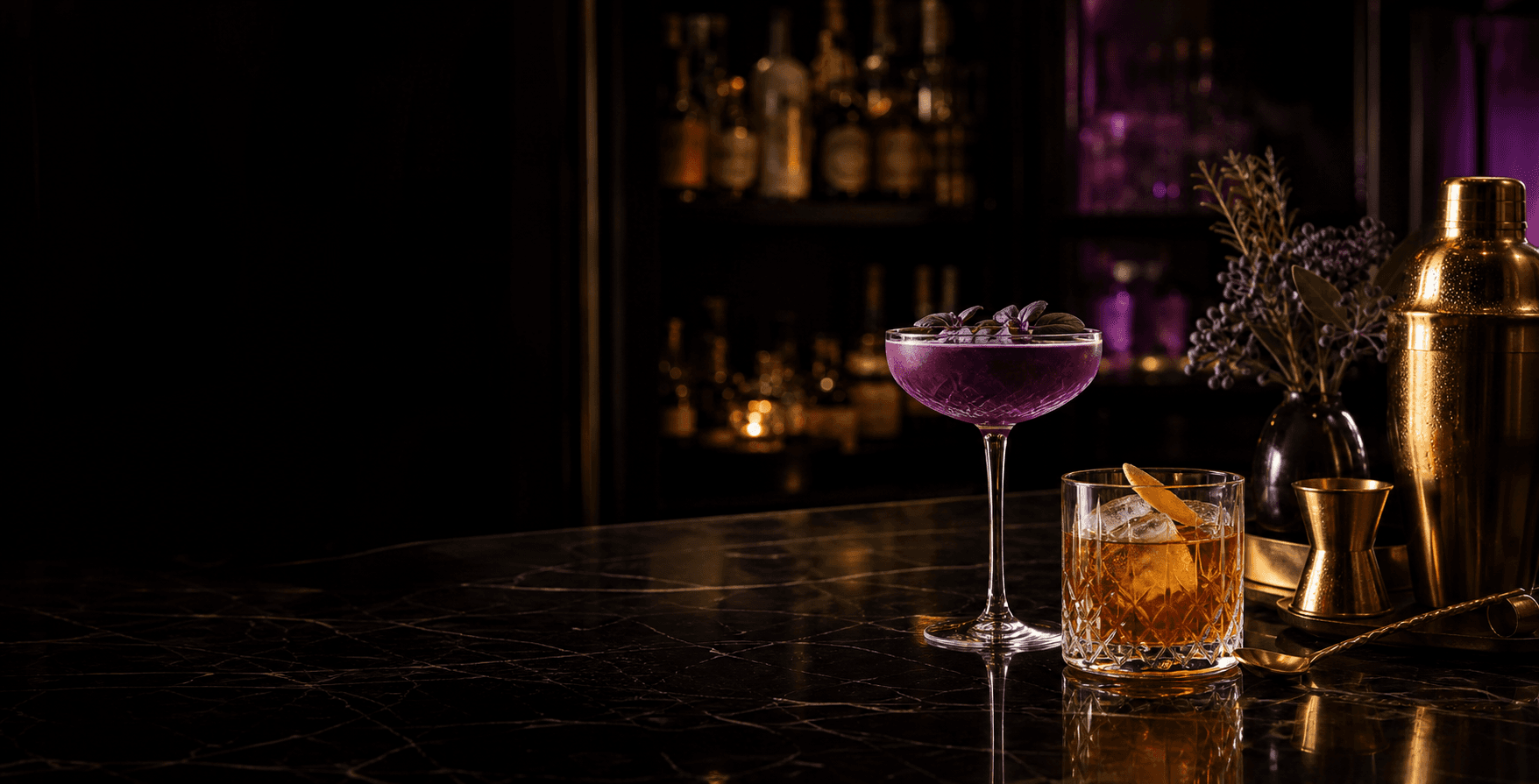 Purple and amber signature cocktails beside polished brass bar tools